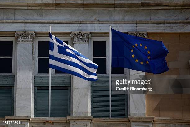 Greek national flag, left, flies beside a European Union flag in Athens, Greece, on Monday, March 31, 2014. The European Commission predicts the...