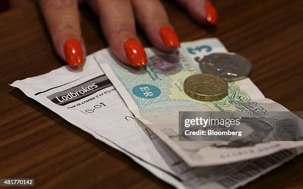 An employee passes a customer their winnings at the counter inside a branch of Ladbrokes Plc bookmakers, in London, U.K., on Friday, July 24, 2015....