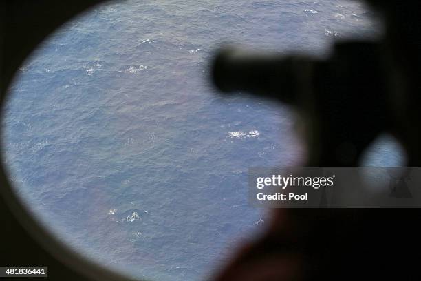 An observer on a Japan Coast Guard Gulfstream aircraft takes photos out of a window while searching for wreckage and debris of missing Malaysia...