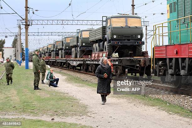 Woman walks past a trainload of KAMAZ Russian military trucks after their arrival at Ostryakovo railway station, some 20 km outside near the Crimean...