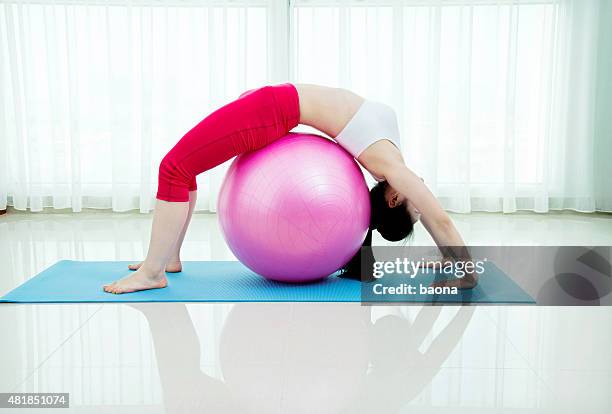 mujer joven de estiramiento en pelota de ejercicio - yoga ball fotografías e imágenes de stock