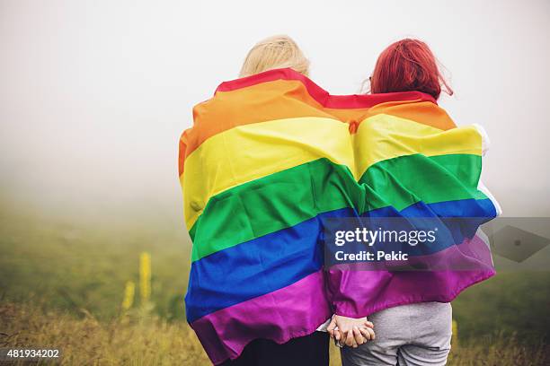 blonde and redhead woman wrapped in rainbow flag - gay flag stockfoto's en -beelden