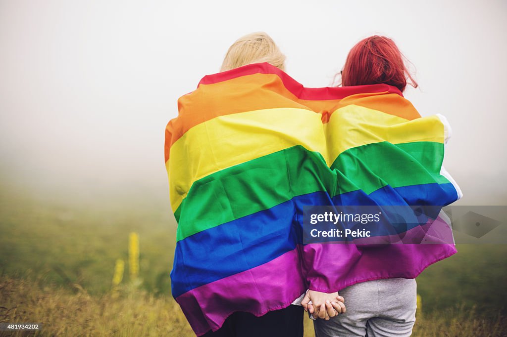 Blonde and redhead woman wrapped in rainbow flag