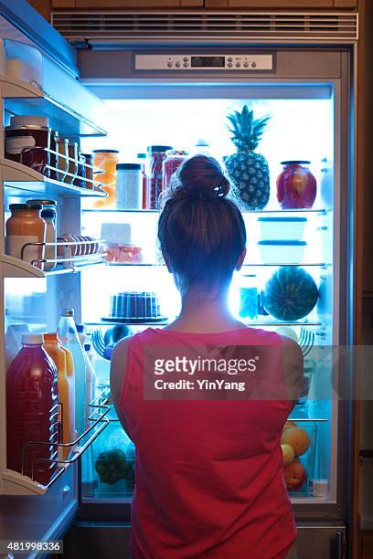 woman contemplating midnight snack late night with open refrigerator - refrigerator stock pictures, royalty-free photos & images