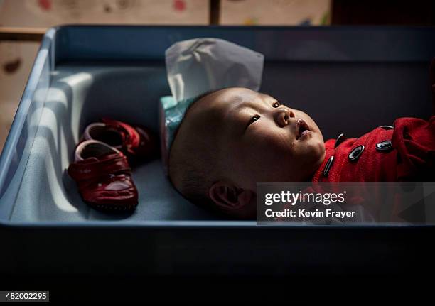Young orphaned Chinese girl lays on a changing table at a foster care center on April 2, 2014 in Beijing, China. China's orphanages and foster homes...