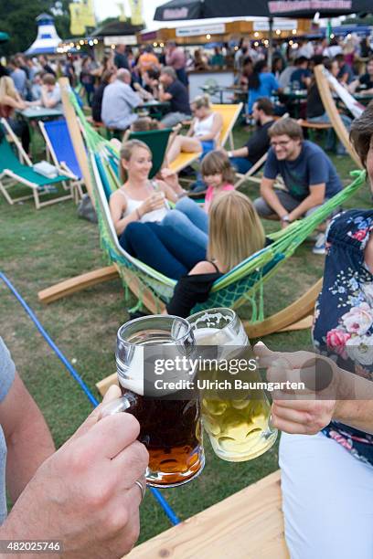 Beer festival in the Bonn Rheinaue leisure park. Toasting with filled beer glasses. In the background young woman in a hammock.