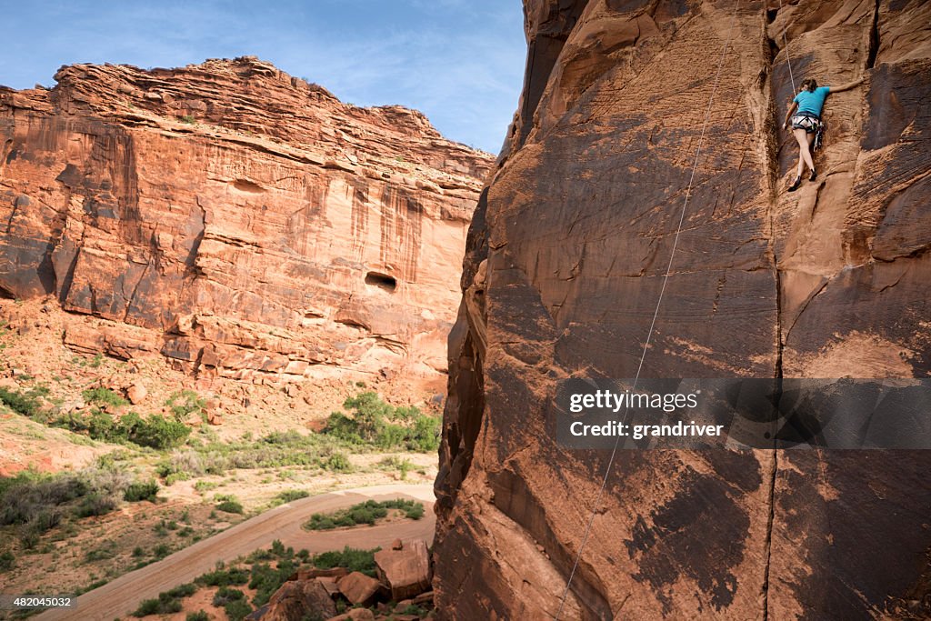 Young Caucasian WomanClimbing a Sheer Cliff of Red Sandstone