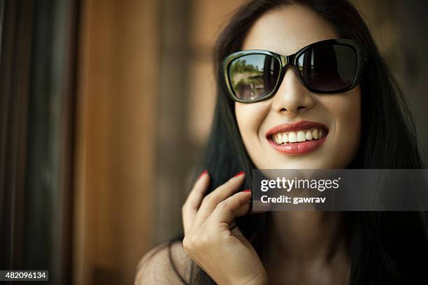attraktive, glückliche junge frau in sonnenbrille für offenes lächeln. - bright smile stock-fotos und bilder