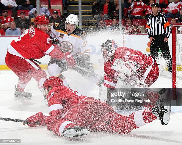 Jimmy Howard of the Detroit Red Wings makes a save on Jordan Caron of the Boston Bruins while teammates Justin Abdelkader and Brian Lashoff defend...