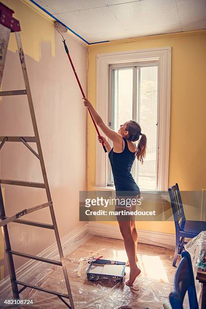 Young woman painting walls with an extended rollerbrush.
