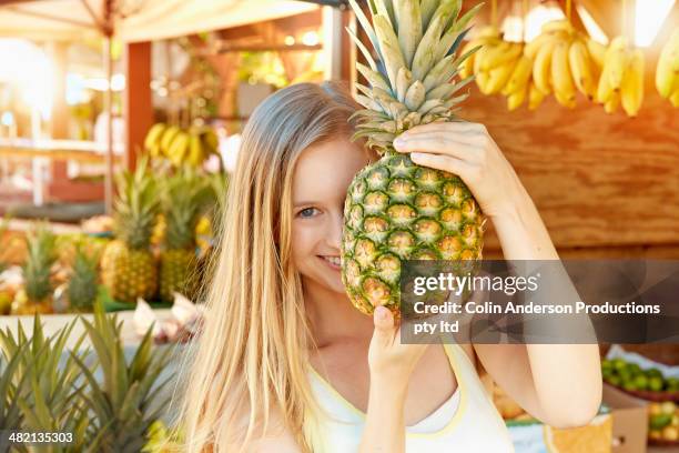 caucasian woman holding pineapple at produce stand - market stall stock pictures, royalty-free photos & images