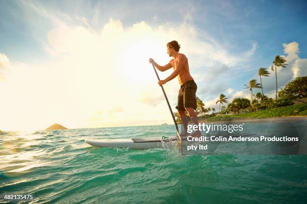 caucasian man on paddle board in ocean - paddle board men imagens e fotografias de stock