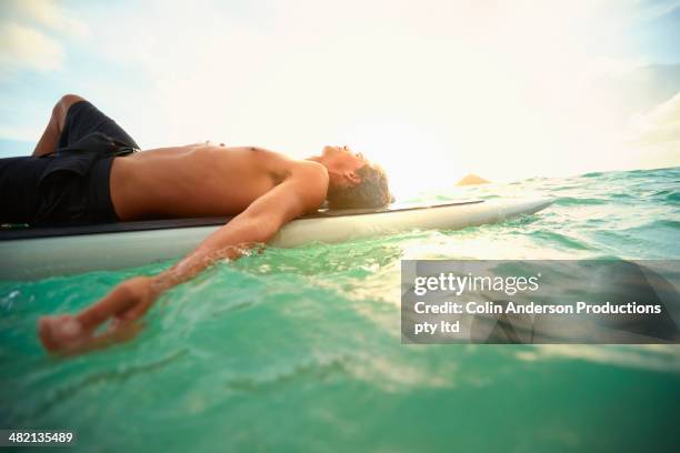 caucasian man laying on paddle board in ocean - paddle board men imagens e fotografias de stock