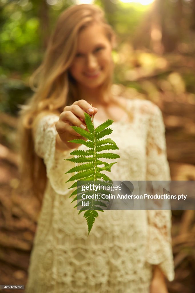 Caucasian woman holding fern leaf in woods