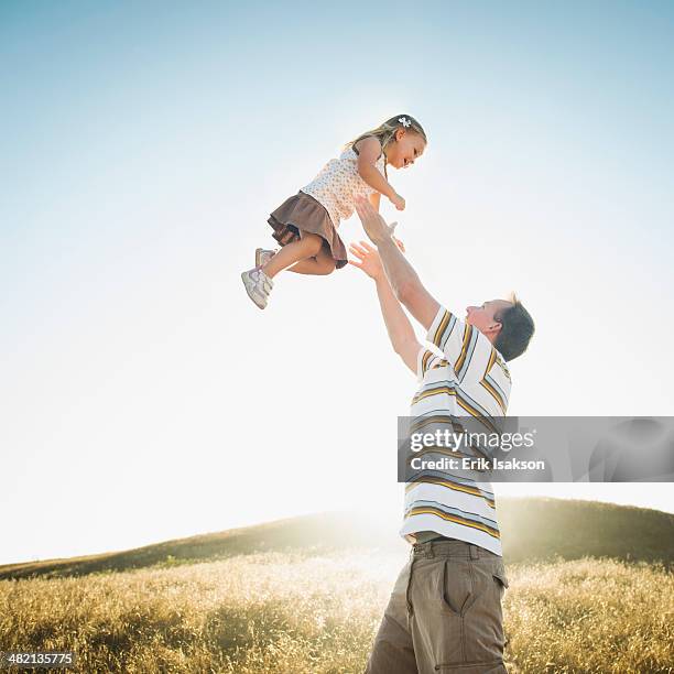 caucasian father lifting daughter overhead in rural field - arremessar imagens e fotografias de stock