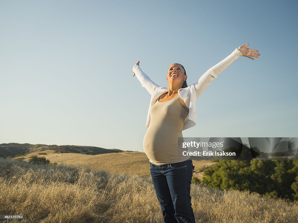 Pregnant Hispanic mother stretching in rural field