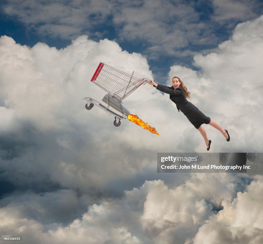 Caucasian businesswoman flying on shopping cart in clouds