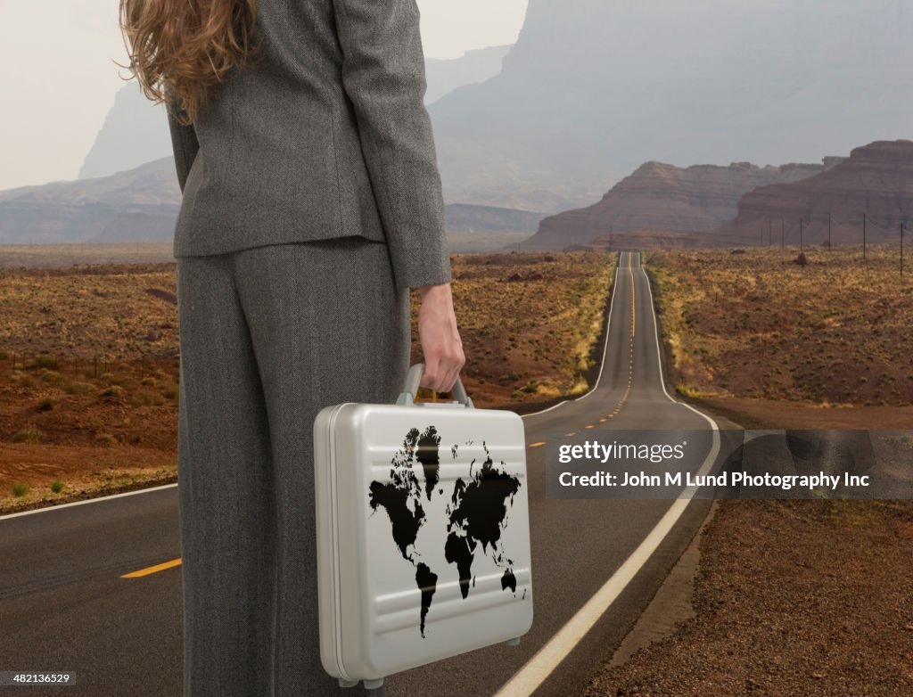 Caucasian businesswoman with world briefcase on open road