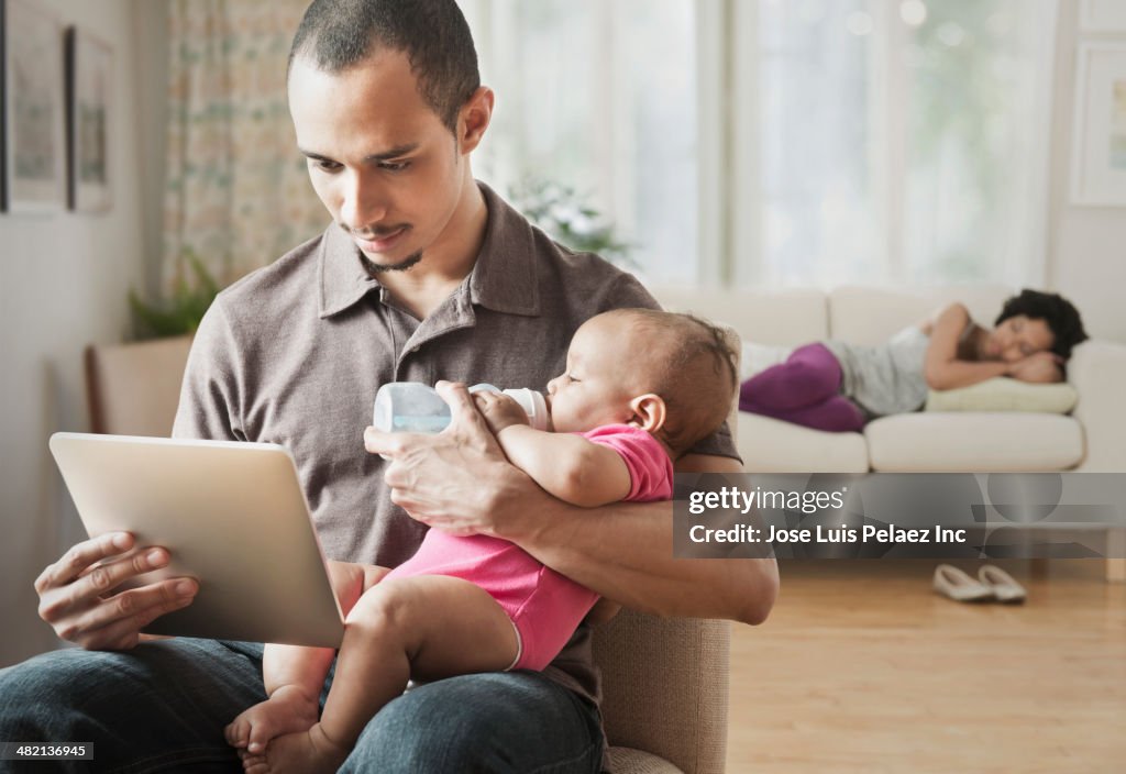 Father feeding baby and using digital tablet