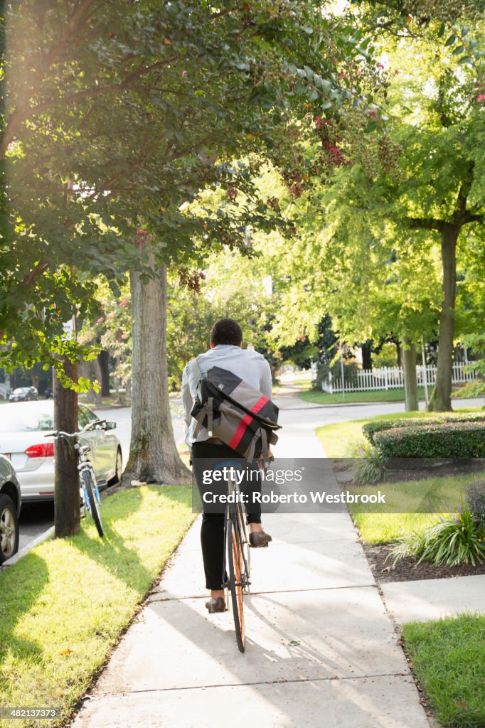Mixed race man riding bicycle on suburban sidewalk