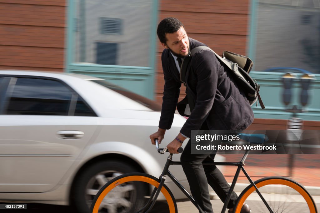 Mixed race businessman riding bicycle on city street