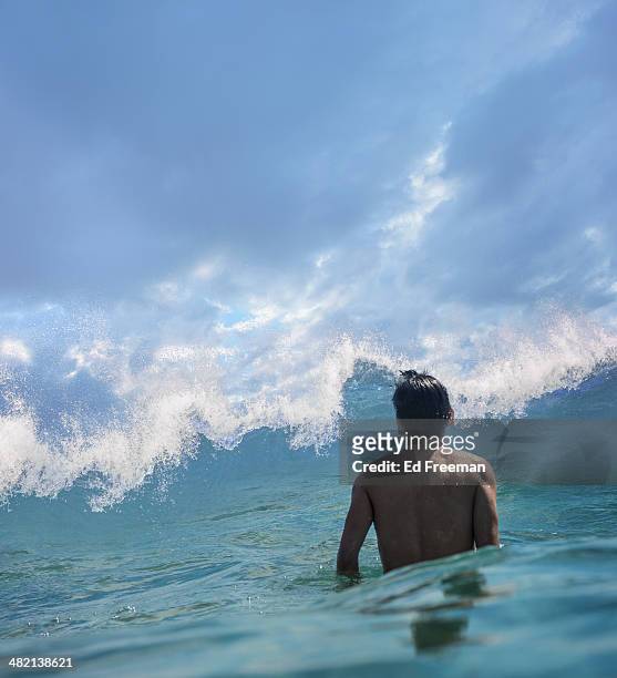 young man in water facing big wave - nähern stock-fotos und bilder