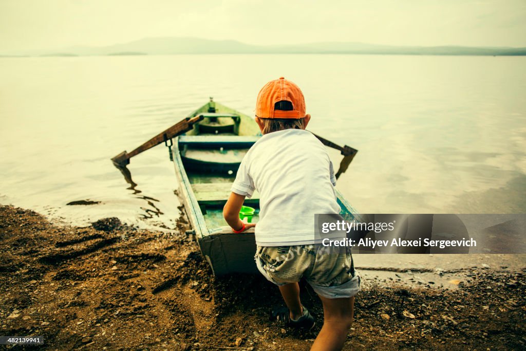 Caucasian boy pushing boat into still lake