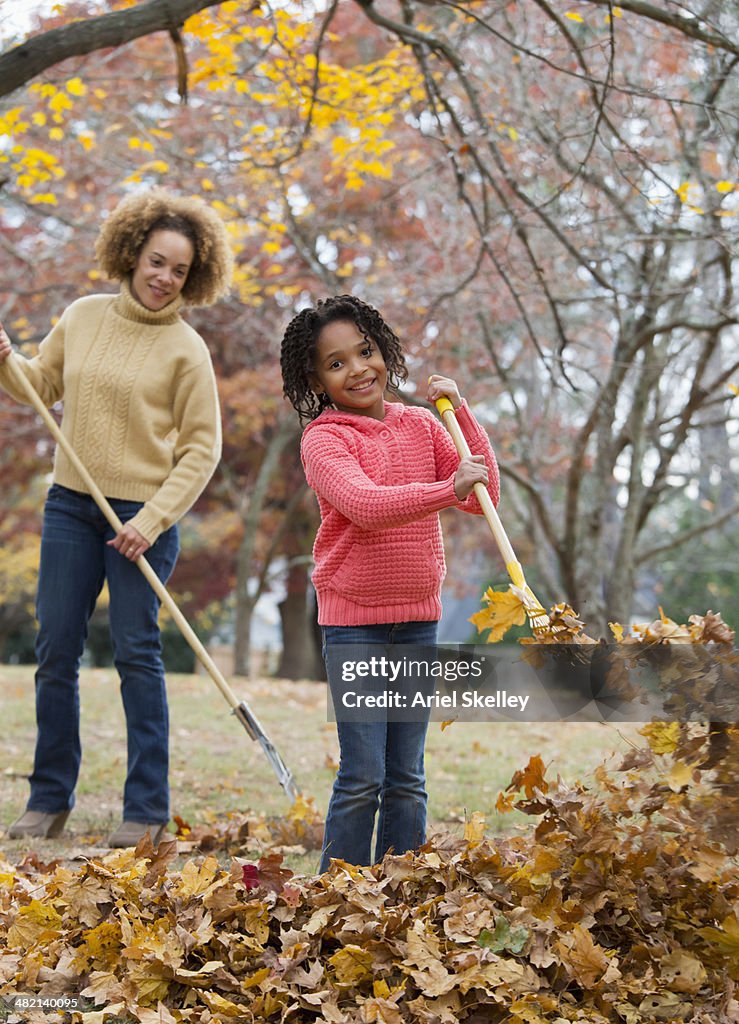 Black mother and daughter raking autumn leaves