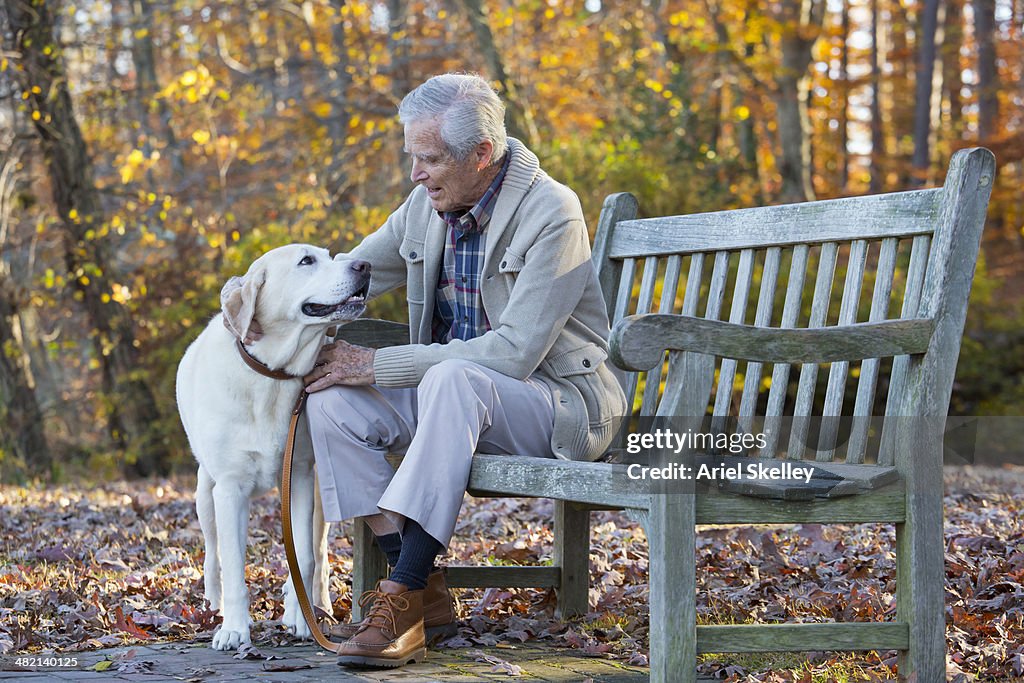 Senior Caucasian man petting dog on park bench