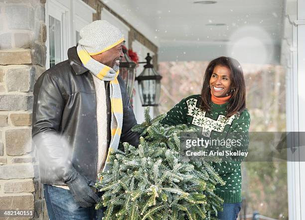 couple carrying fresh cut christmas tree on porch - christmas tree 50's stockfoto's en -beelden