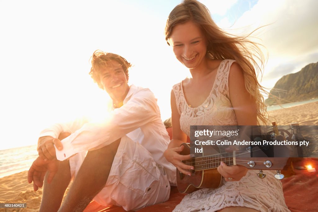 Caucasian woman playing ukulele for boyfriend on beach