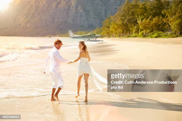 caucasian couple running on beach - rico e anderson fotografías e imágenes de stock