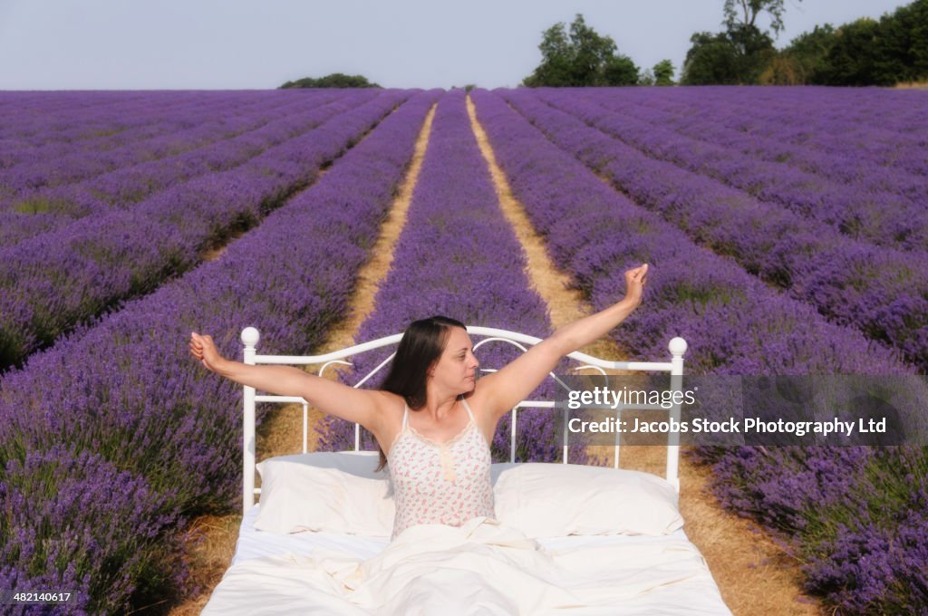 Hispanic woman waking in bed in lavender field