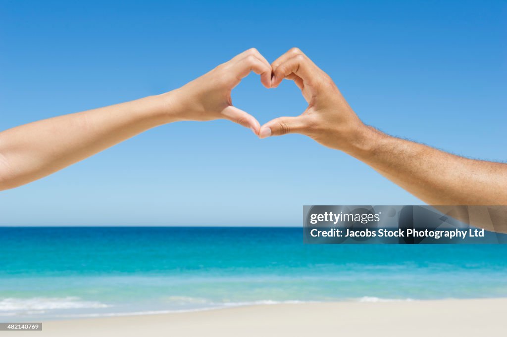 Mixed race couple making heart-shape with hands on beach