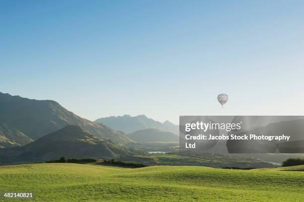 hot air balloon flying above rolling landscape - balloons in sky stock pictures, royalty-free photos & images