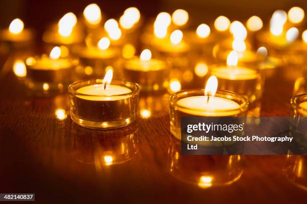 close up of lit tea light candles on wooden table - kerzenschein stock-fotos und bilder
