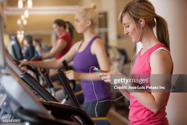 caucasian woman using mp3 player on elliptical trainer in gym - happy caucasian woman on elliptical trainer at gym stock pictures, royalty-free photos & images