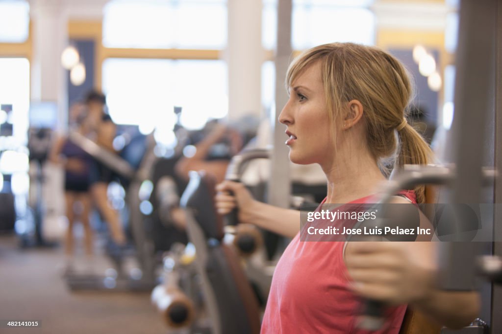 Caucasian woman using weight machine in gym