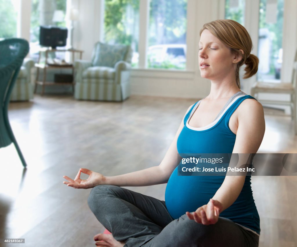 Pregnant Caucasian woman meditating in living room