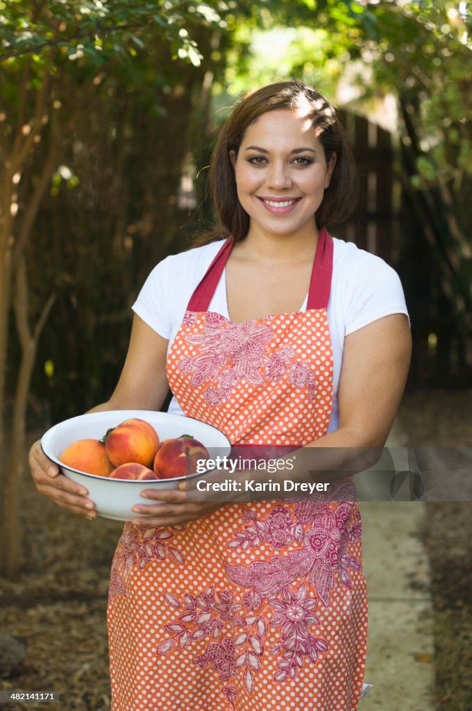 Mixed race woman holding bowl of peaches outdoors