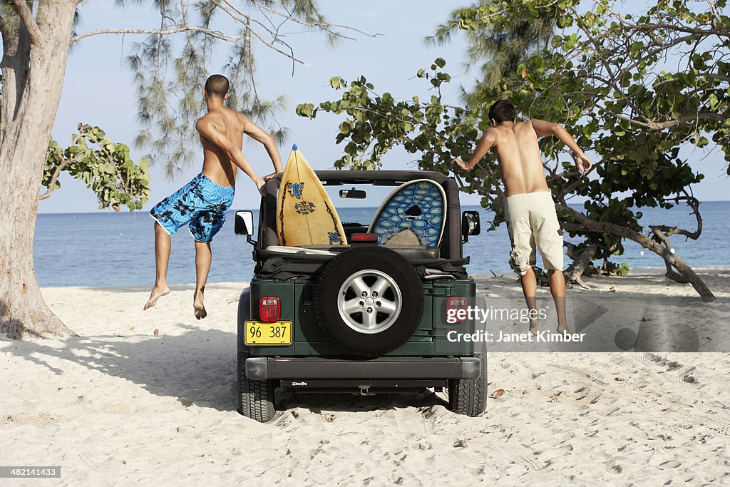 Surfers jumping out of 4x4 with surfboards on beach