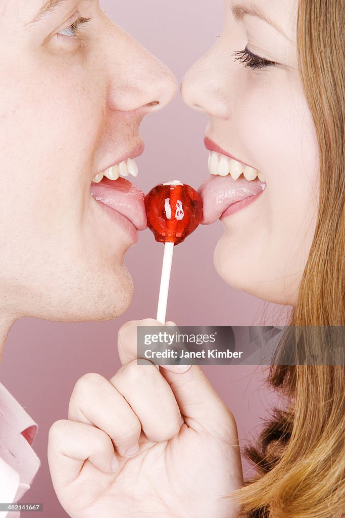 Caucasian couple licking lollipop