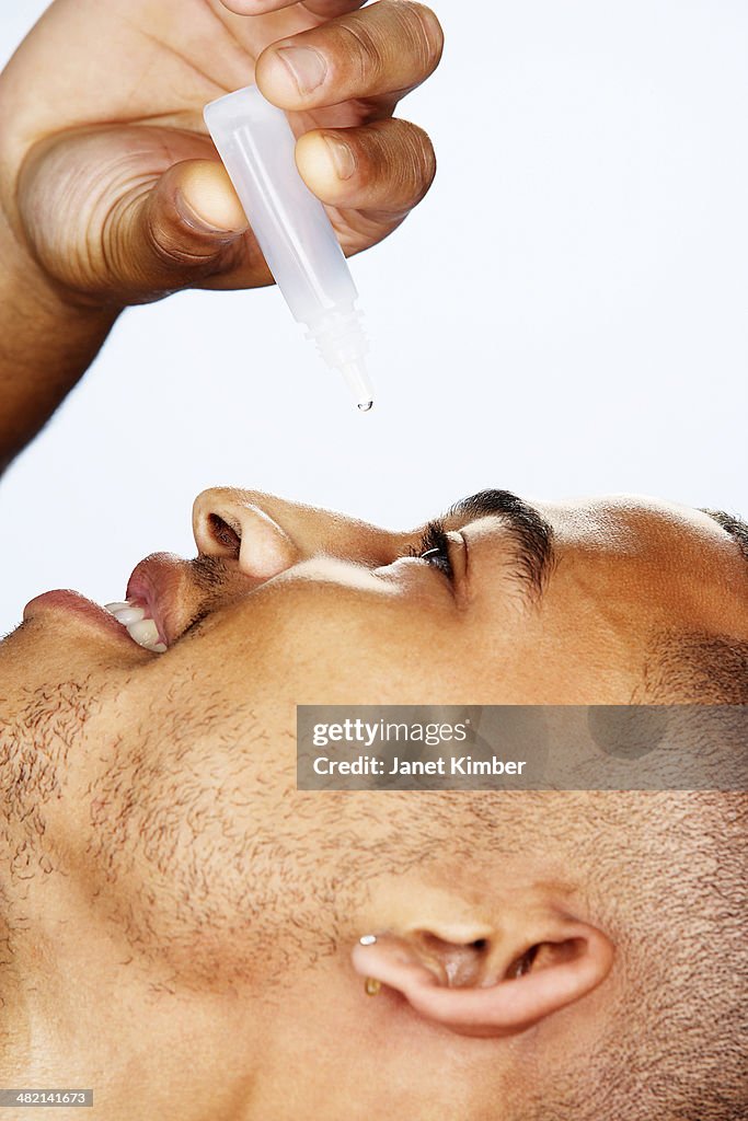 Mixed race man putting in eye drops