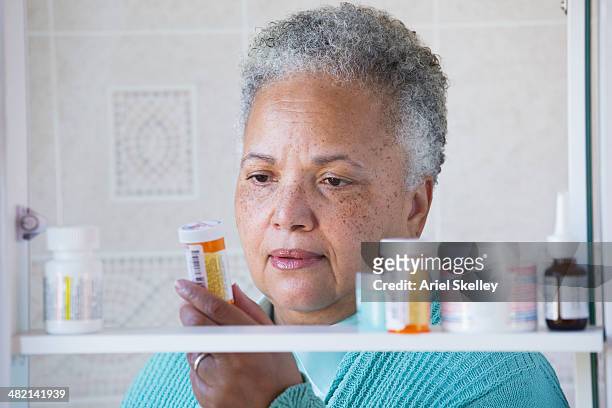 black woman examining prescription bottle in medicine cabinet - bathroom cabinet stock pictures, royalty-free photos & images