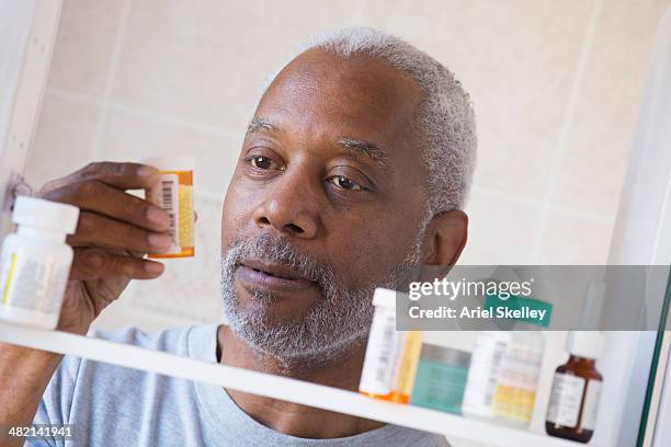 black man examining prescription bottle in medicine cabinet - armário de banheiro - fotografias e filmes do acervo