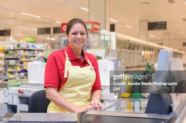 portrait of smiling hispanic woman working at grocery checkout - female supermarket stock-fotos und bilder