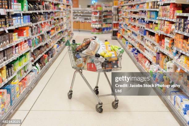 full shopping cart in supermarket aisle - cheio imagens e fotografias de stock