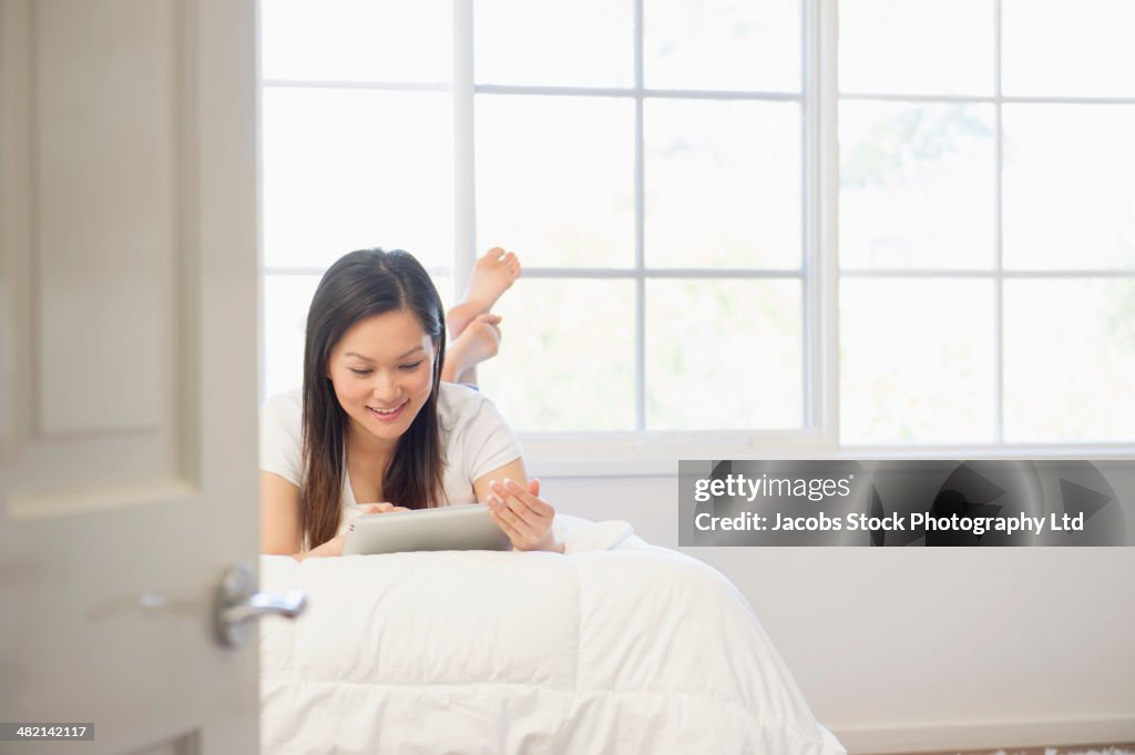 Chinese woman using digital tablet on bed