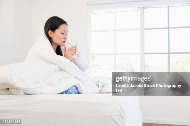 chinese woman with coffee wrapped in a blanket on bed - wrapped in a blanket stock pictures, royalty-free photos & images