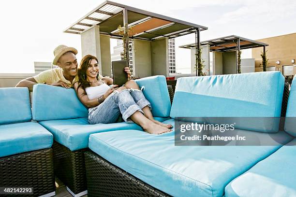 couple using digital tablet on sofa on urban rooftop - tablet paar sommer stock-fotos und bilder